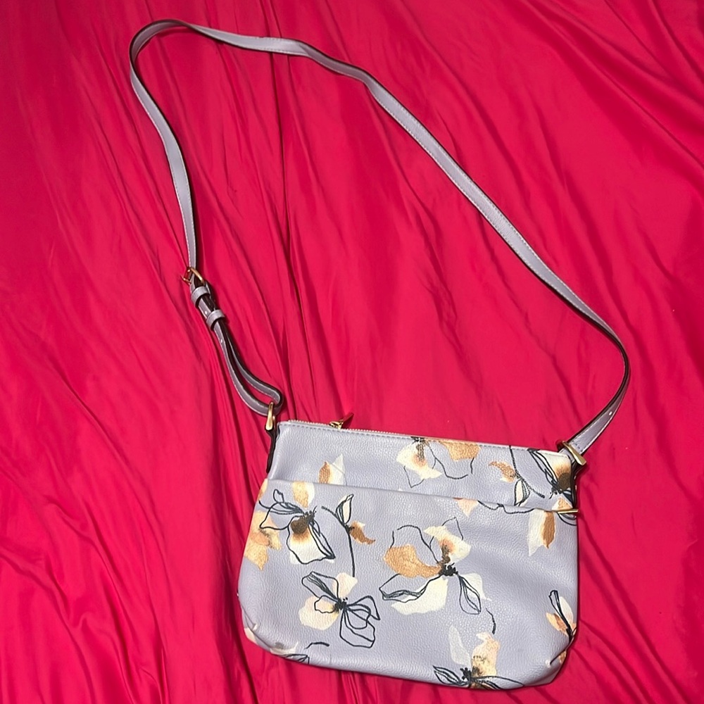 A blue cross body purse with white flowers on it